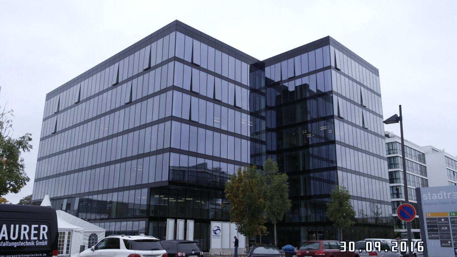 A modern glass office building with reflective windows, surrounded by parked cars and trees. The date 30.09.2016 is displayed in the lower right corner of the image.