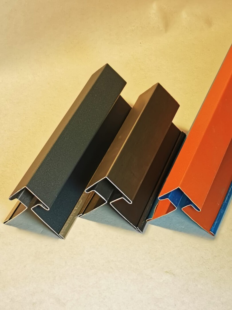 Vier Metallprofile mit Z-Profil, nebeneinander angeordnet auf einer hellen Fläche. Drei sind dunkelgrau oder braun, eines leuchtend orange mit blauer Innenseite.