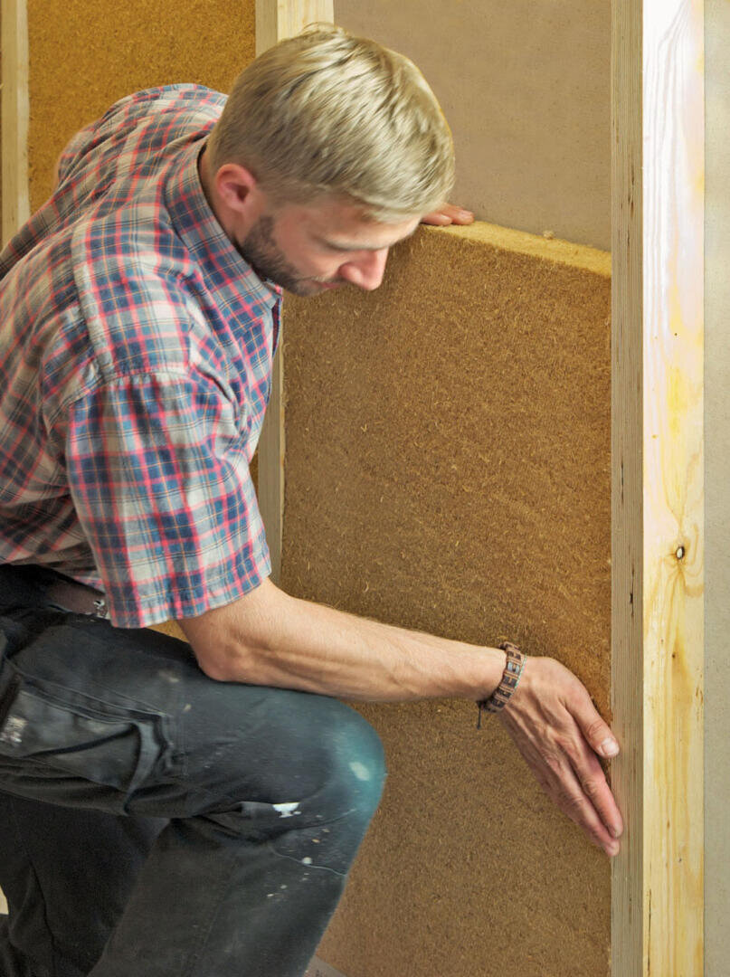 Ein Mann im karierten Hemd installiert eine Platte aus natürlichem Isoliermaterial in einem Holzrahmen und drückt sie mit seinen Händen an ihren Platz.