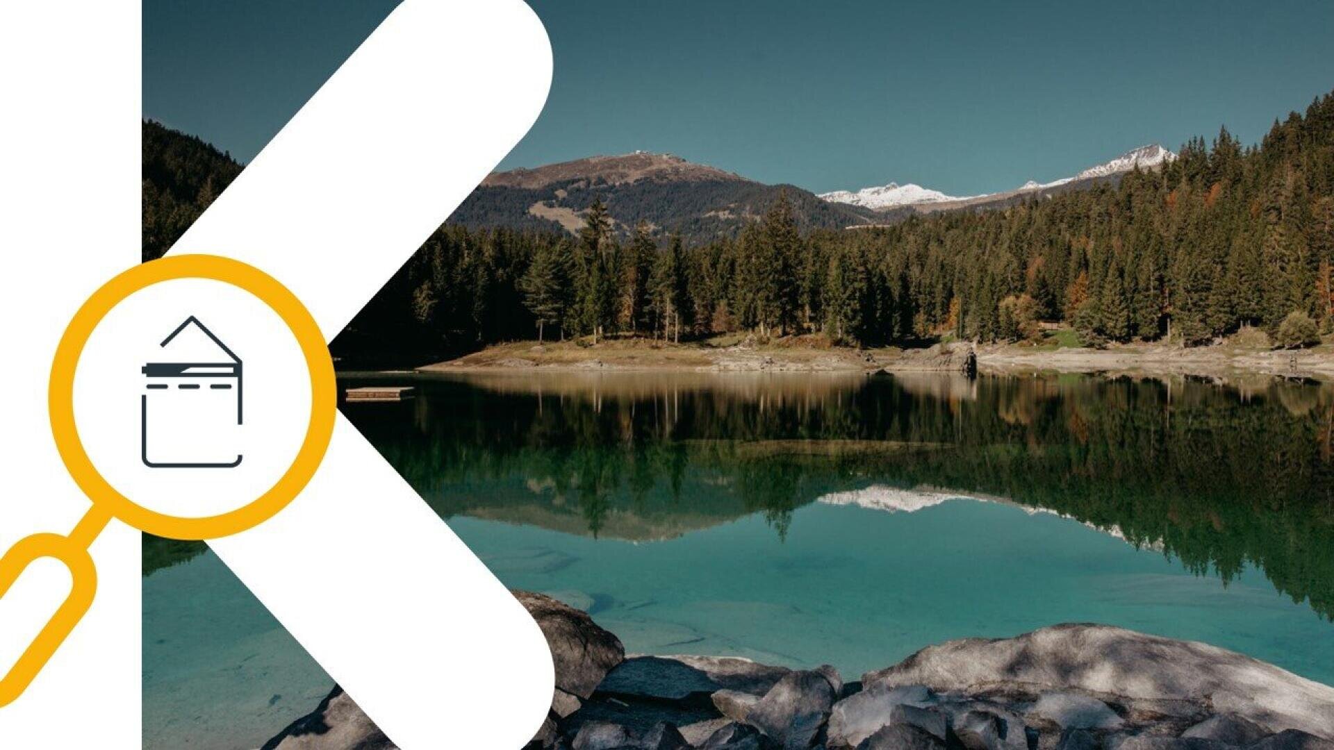 A clear lake surrounded by pine trees and mountains under a blue sky, with snow-capped peaks in the distance. A large white letter K and a yellow magnifying glass graphic overlay part of the image.