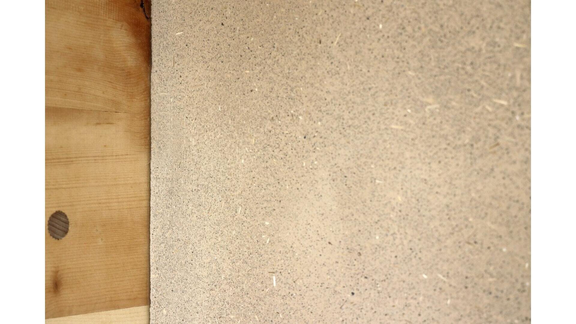Close-up of a textured beige surface, possibly a concrete or plaster wall, next to a smooth, light wooden panel with a visible knot. The surfaces meet at a vertical edge on the left side of the image.