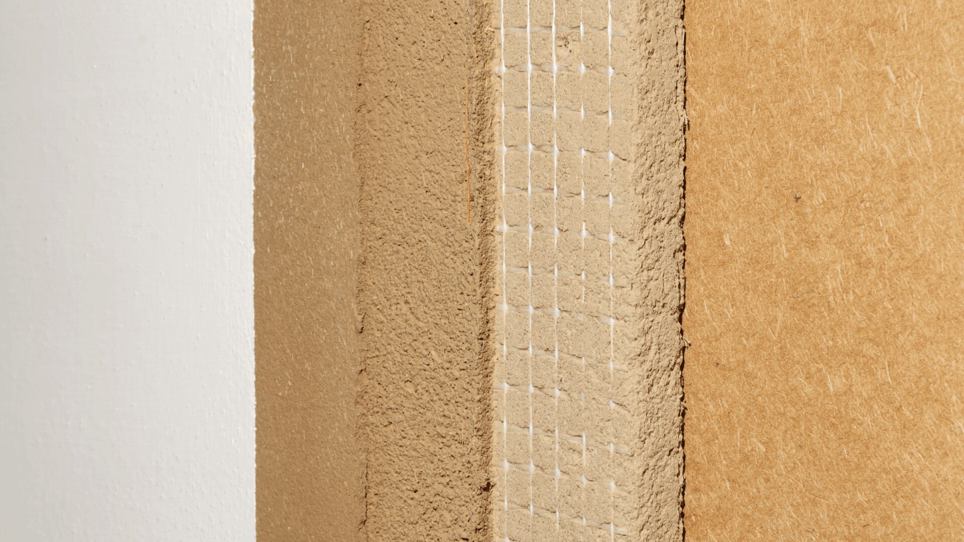 Nahaufnahme der Kante einer Wand oder Platte mit Schichten aus strukturierten, beigen und braunen Materialien, einschließlich eines Abschnitts mit einem Gittermuster und rauen, unbearbeiteten Oberflächen.