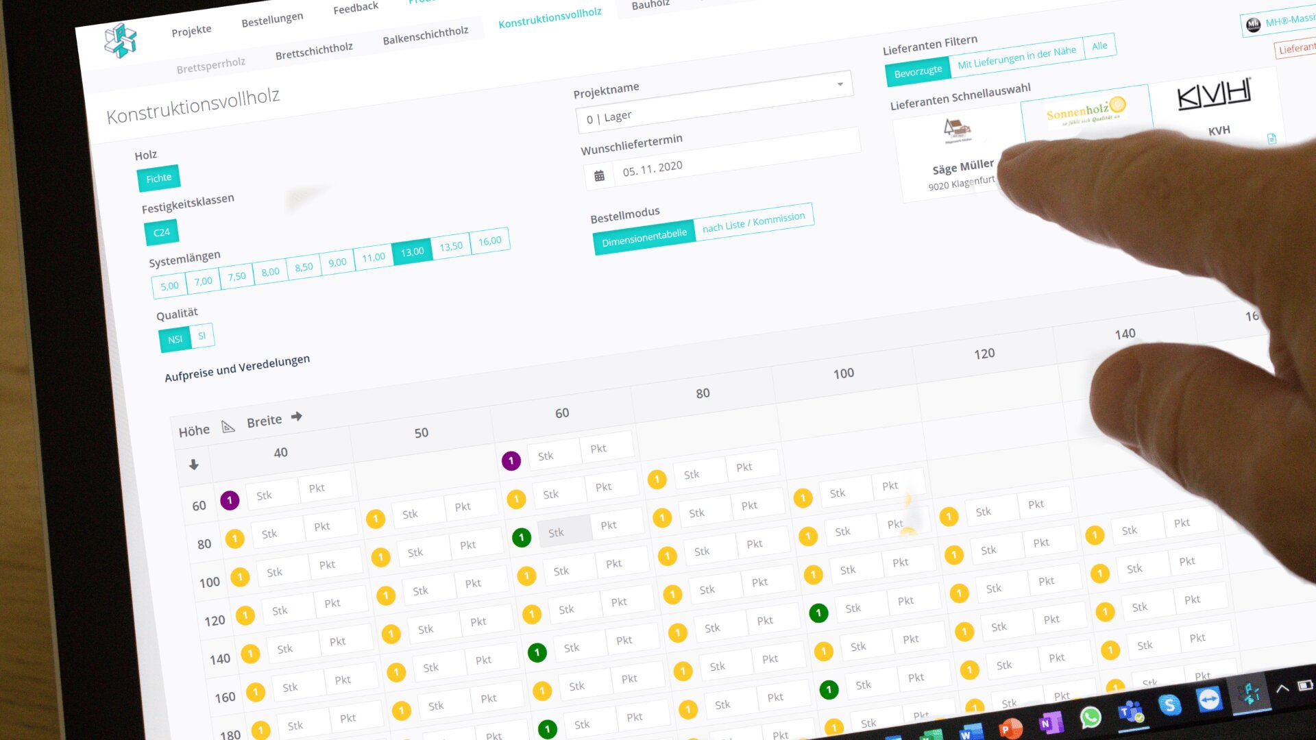 Die Hand einer Person zeigt auf einen Computerbildschirm, auf dem ein Bestellformular für Holzbauarbeiten mit verschiedenen Feldern, Filtern sowie einer Tabelle mit Preisen und Lieferanten angezeigt wird. Die Benutzeroberfläche ist auf Deutsch.