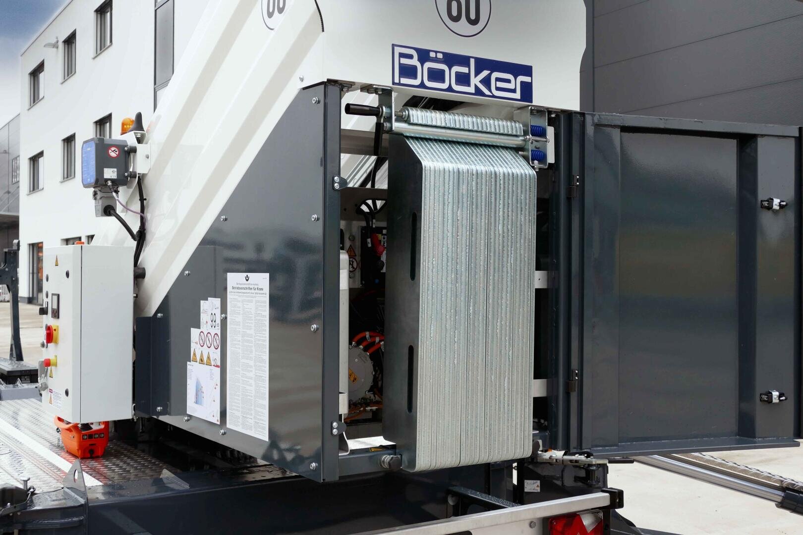 Close-up of an industrial machine with an open compartment in which coiled cables can be seen. The machine bears the Böcker brand name and is installed outdoors near buildings.