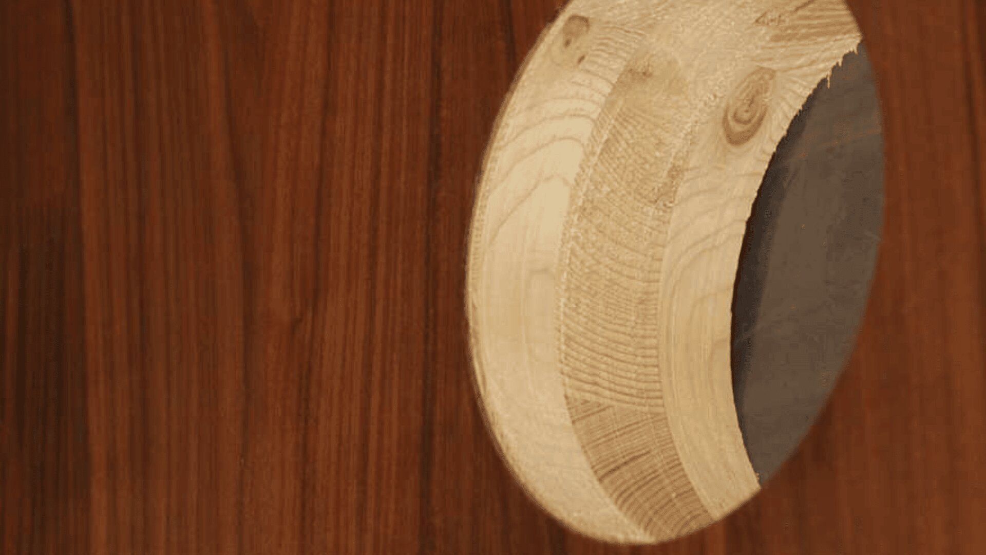 Ein Holzkreis mit einem dunkelgrau schattierten Abschnitt ist in eine polierte Holzoberfläche eingebettet, wodurch ein Kontrast zwischen dem glatten Hintergrund und der strukturierten Maserung des Kreises entsteht.