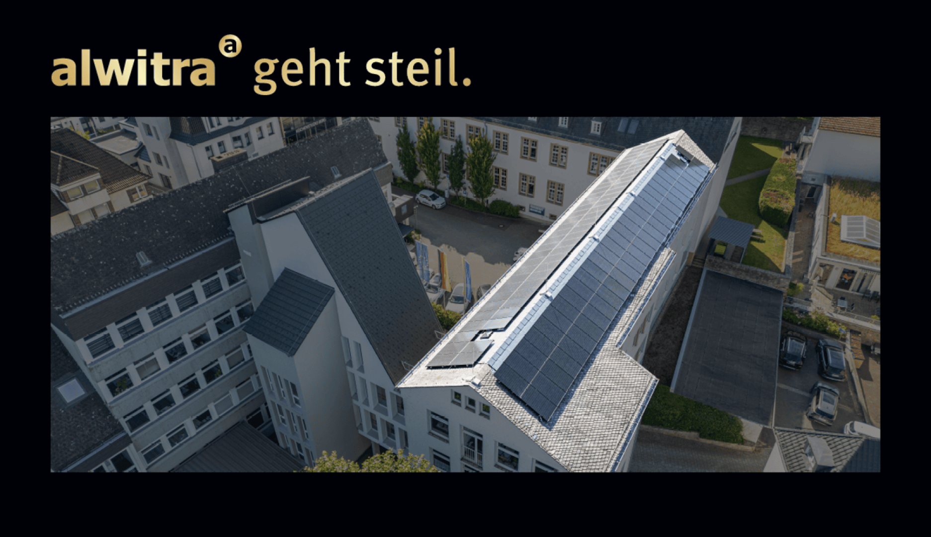 Luftaufnahme eines Gebäudekomplexes mit auf einem Schrägdach installierten Solarzellen; oben links steht "alwitra geht steil." auf schwarzem Hintergrund.