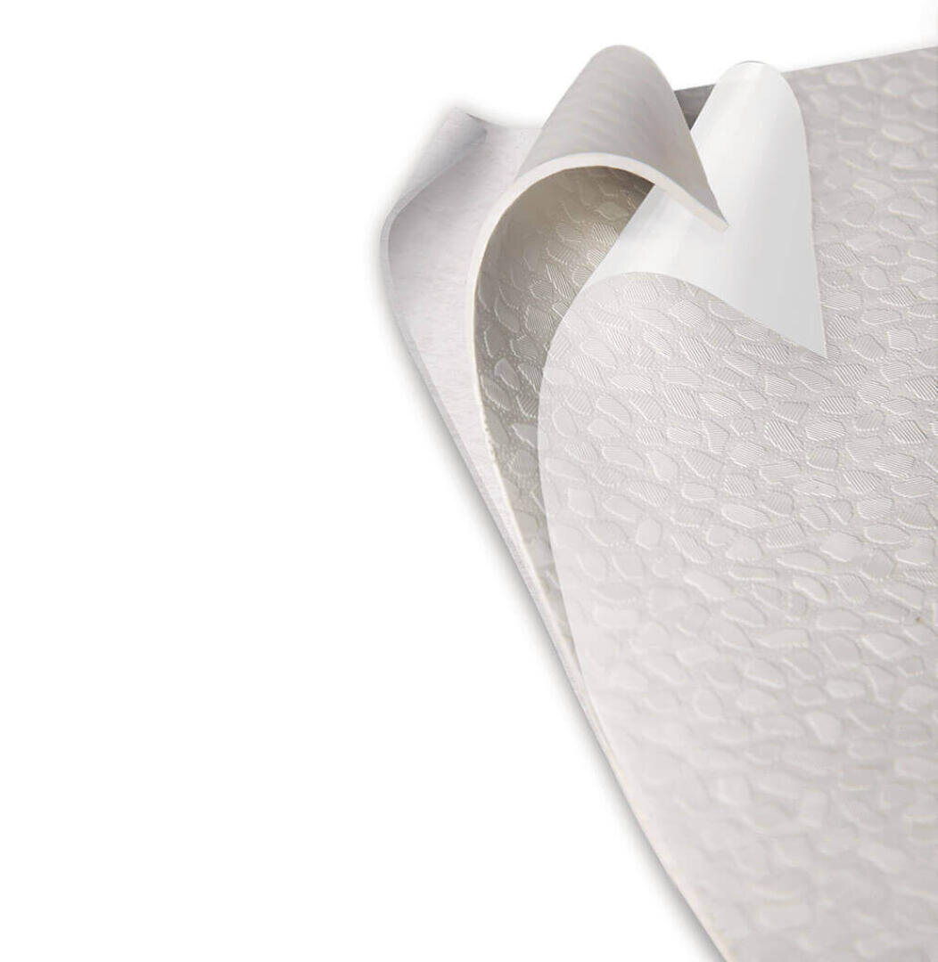 Nahaufnahme einer strukturierten, flexiblen Folie, bei der eine Ecke abgezogen ist und eine klebrige oder selbstklebende Unterseite zum Vorschein kommt. Die Oberfläche weist ein subtiles, sich wiederholendes geometrisches Muster auf.