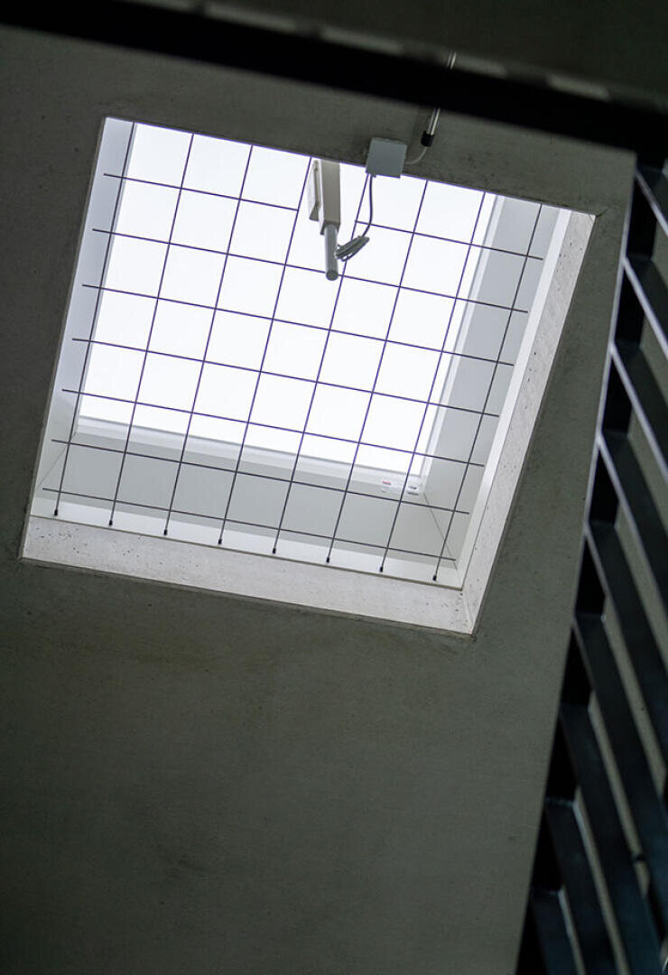 A skylight window with a security grille cover is set into the ceiling and allows natural light to enter. The photo is taken from below, and part of a dark railing can be seen on the right-hand side.