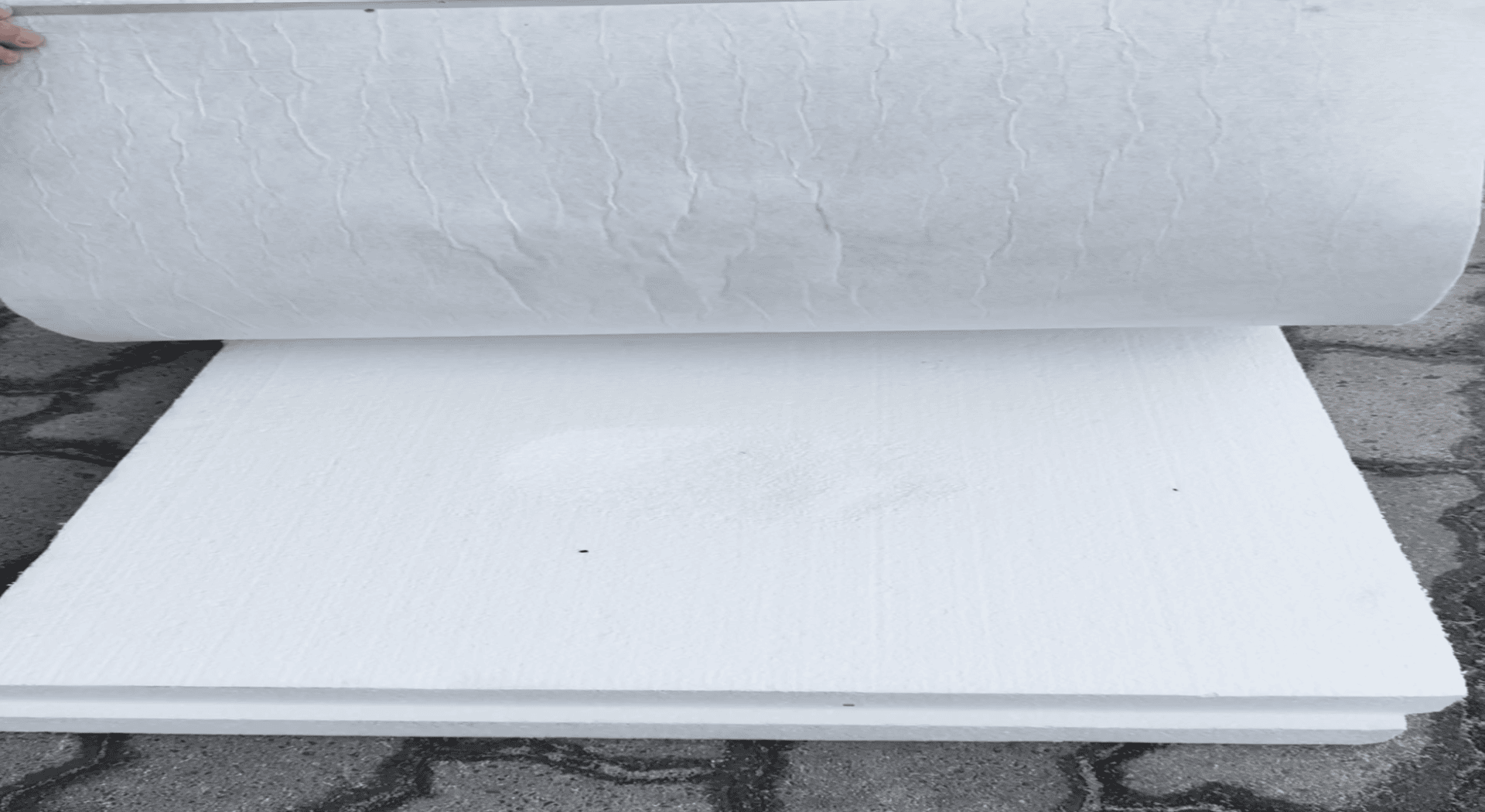 Eine Hand hebt eine große, weiße, flexible Platte von einem Stapel dicker weißer Schaumstoffplatten, die auf einem Steinpflaster liegen.