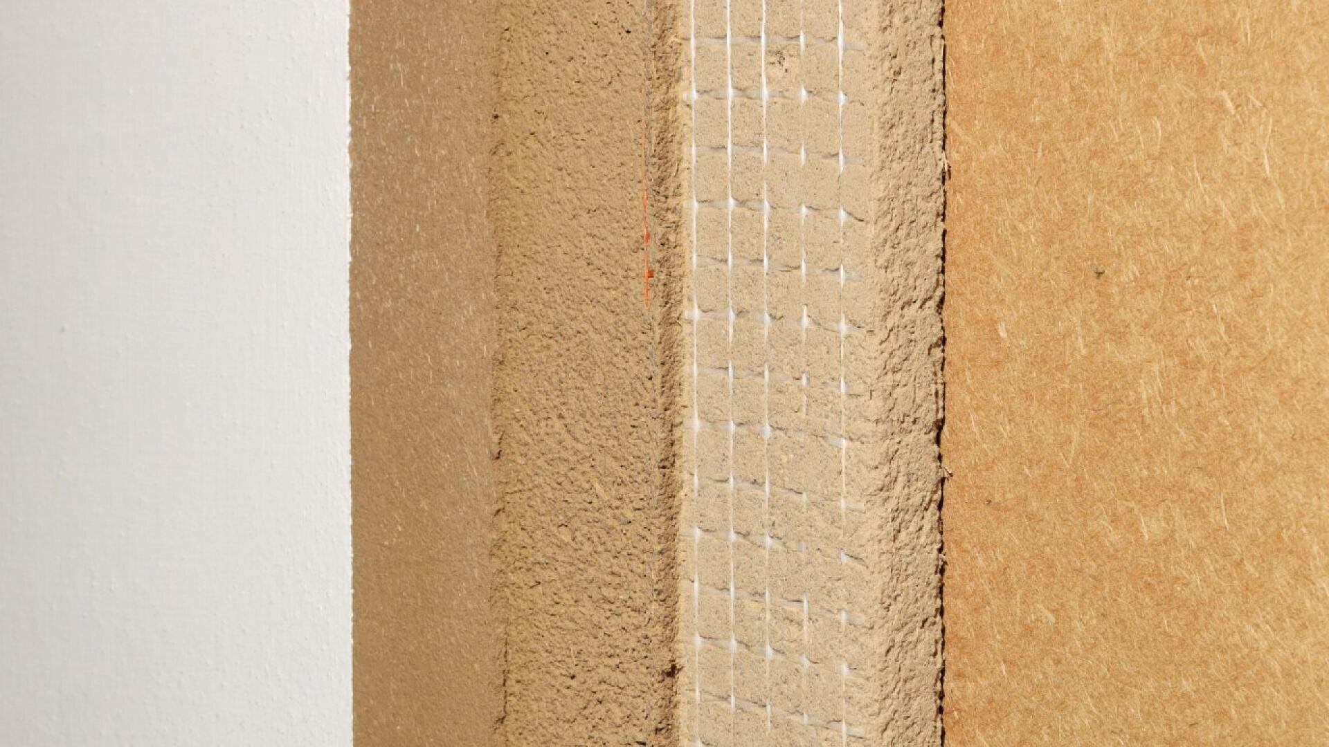 Close-up of the rough edge of a piece of particle board or MDF wood panel against a white wall, showing its layered and textured surface.