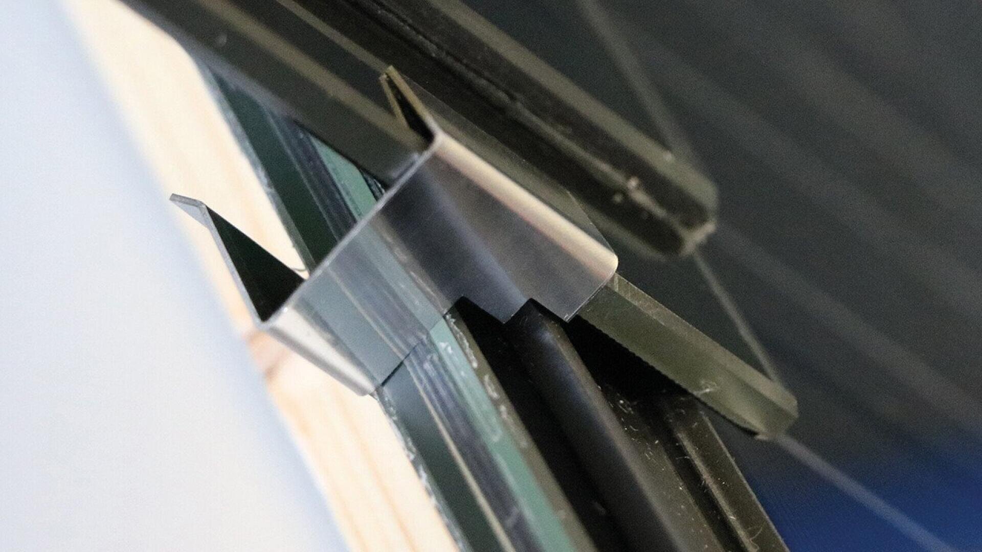 Close-up of a metal clip securing a black panel or frame against a glass and wood structure, showing the clip’s detail and attachment mechanism.