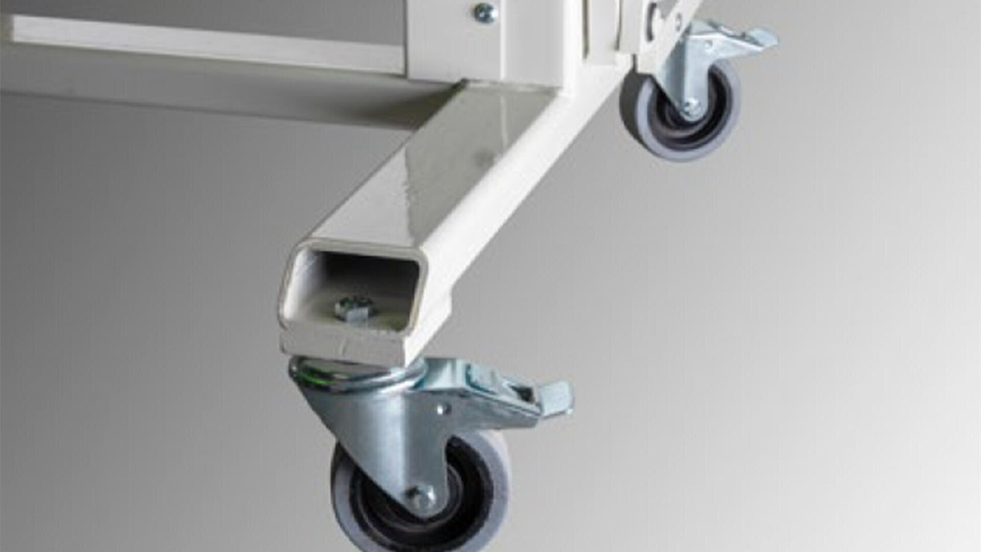 Nahaufnahme von zwei Lenkrollen aus Metall, die am weißen Rahmen eines Möbelstücks oder Geräts befestigt sind, mit einem grauen Hintergrund mit Farbverlauf.