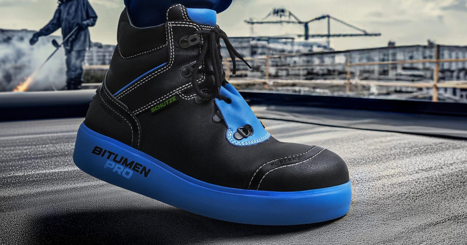 A close-up of a black and blue safety boot with the inscription BITUMEN PRO and an industrial construction site in the background.