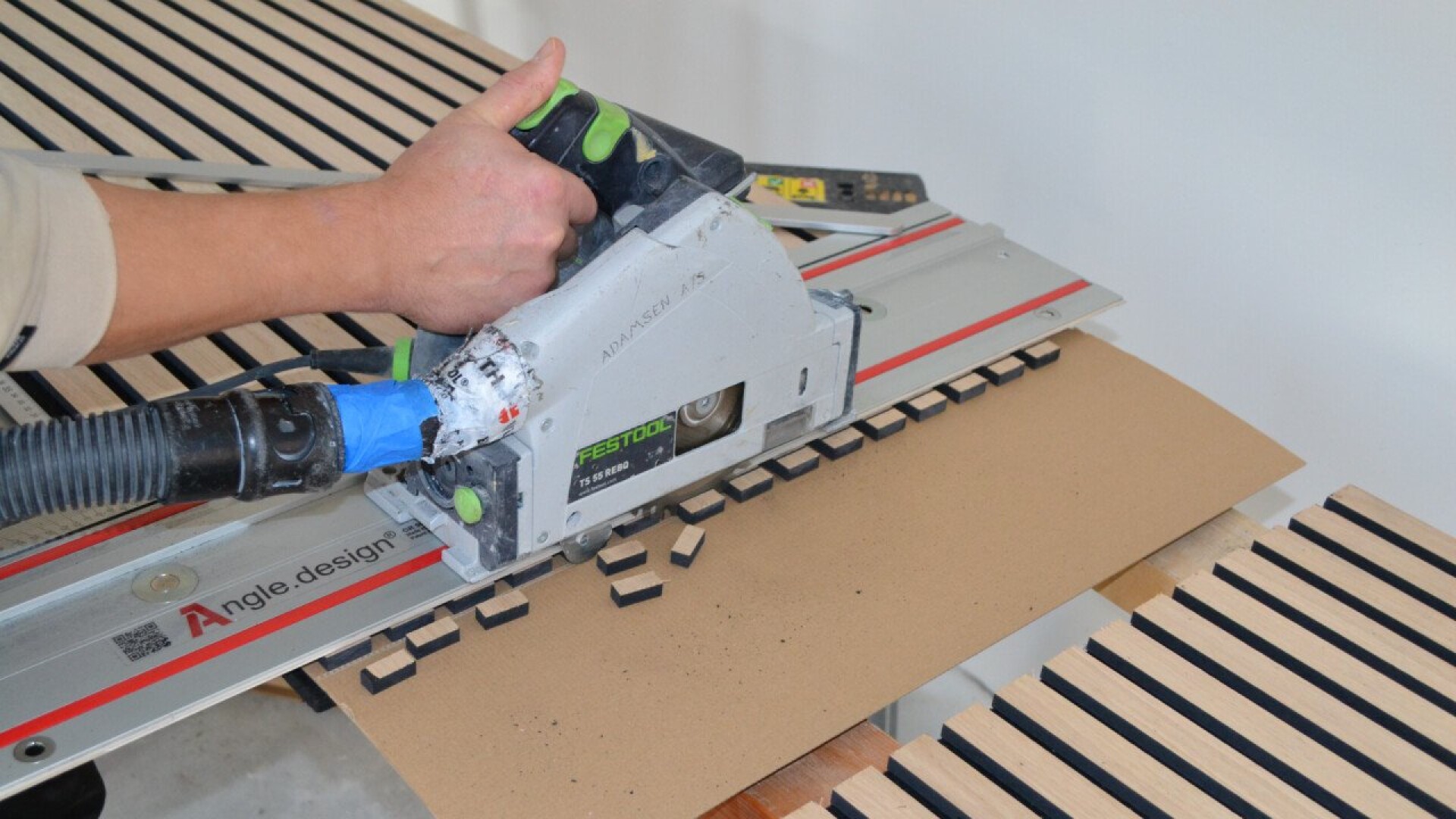 Eine Person verwendet eine Festool-Kreissäge, um gleichmäßig verteilte Lamellen in ein Stück Holz zu schneiden. An der Säge sind eine Schienenführung und ein Staubabsaugschlauch angebracht.