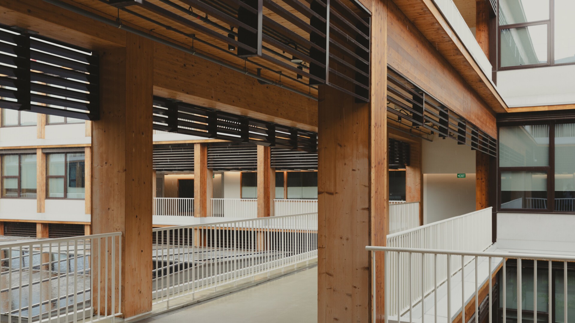 Ein moderner Innenbereich mit Holzbalken, weißem Geländer und großen Fenstern. Das Design zeichnet sich durch klare Linien, Naturholz und eine Mischung aus offenen und geschlossenen Räumen aus.