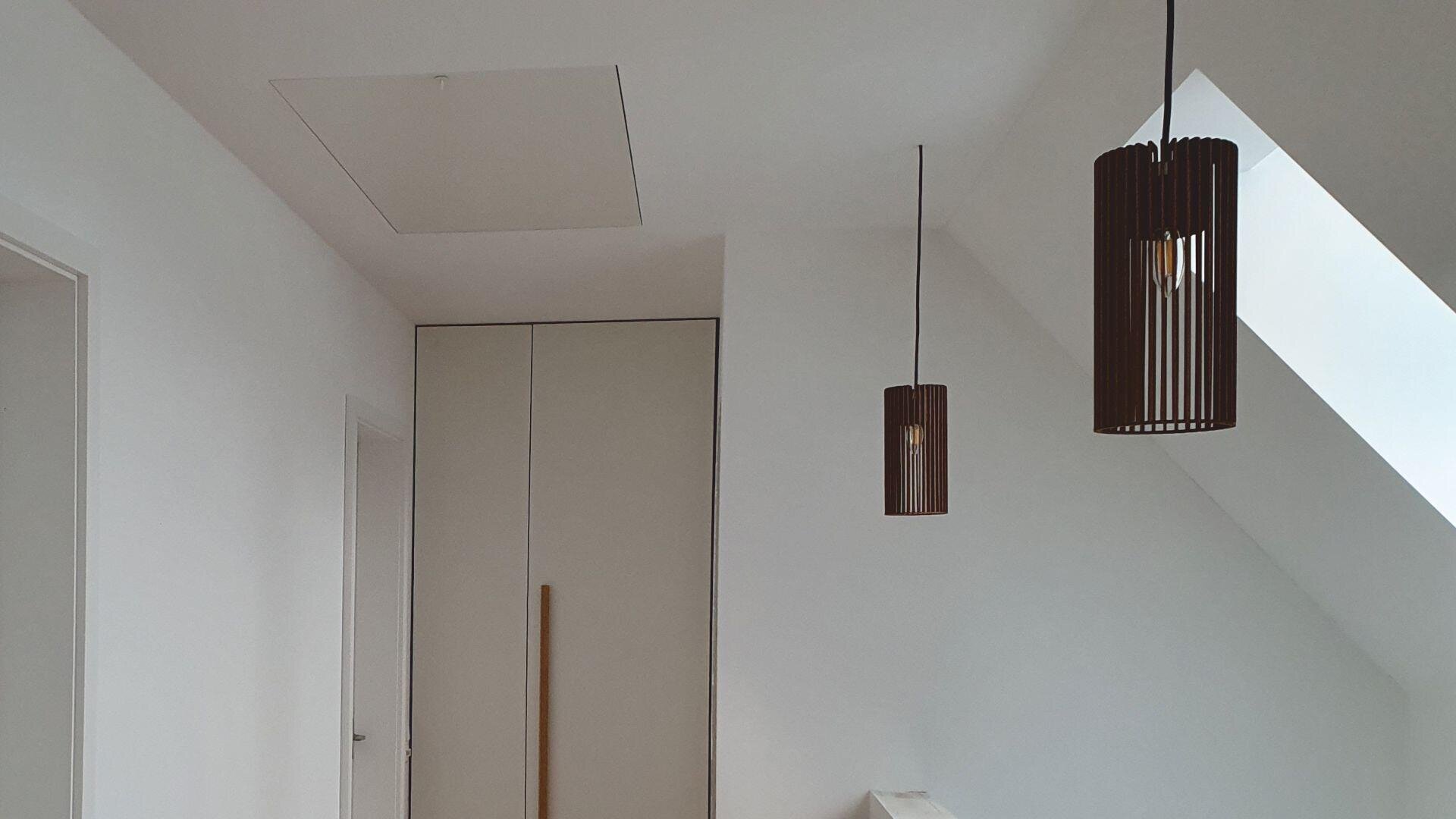 Minimalist interior with white walls, slanted ceiling, two modern pendant lights, a built-in closet, and a skylight letting in natural light. The design is clean and simple.