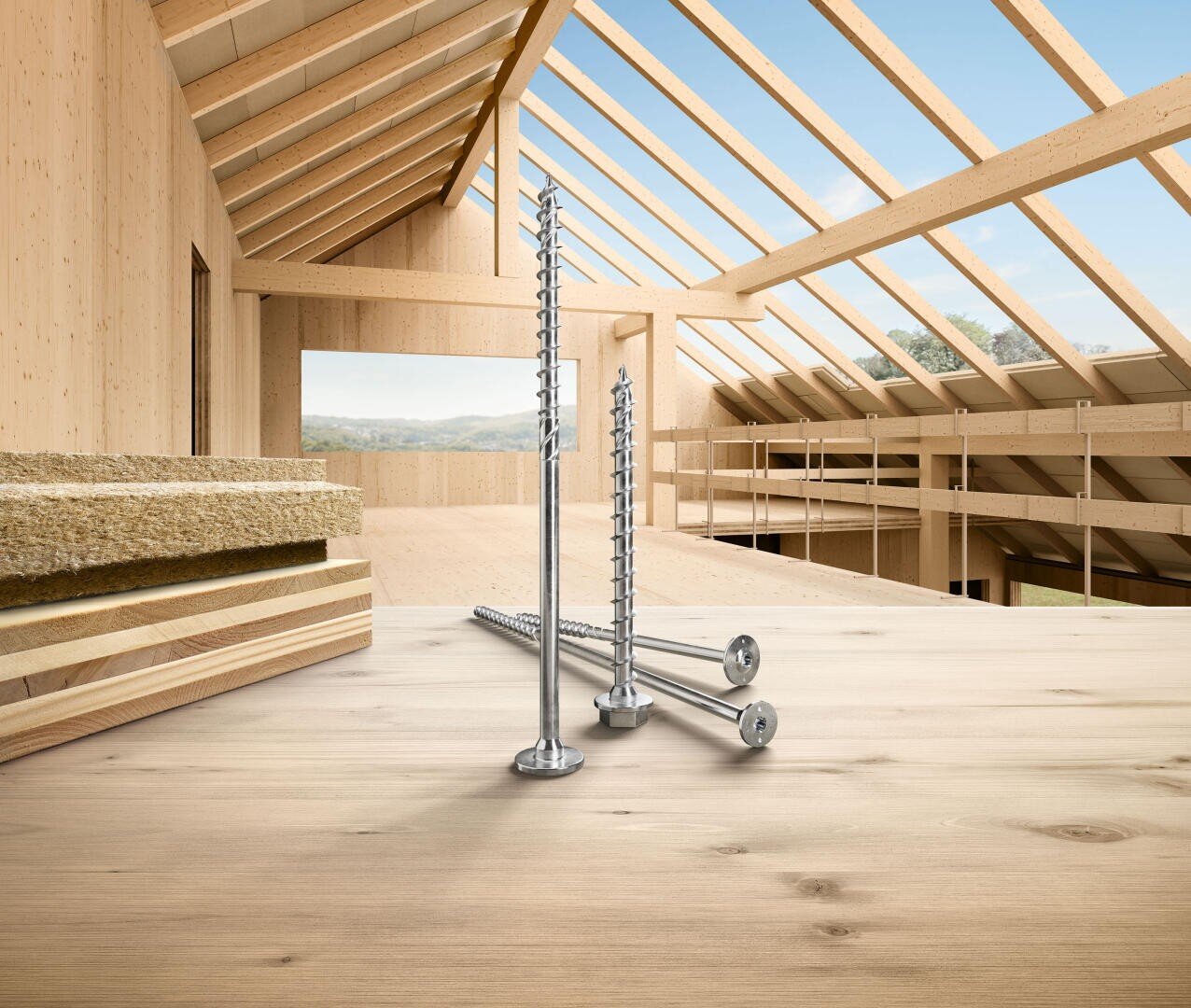 Drei große Metallschrauben stehen aufrecht auf einer hölzernen Oberfläche im Inneren eines teilweise errichteten Holzgebäudes, mit gestapeltem Dämmmaterial auf der linken Seite und freiliegenden Dachbalken über dem Kopf.