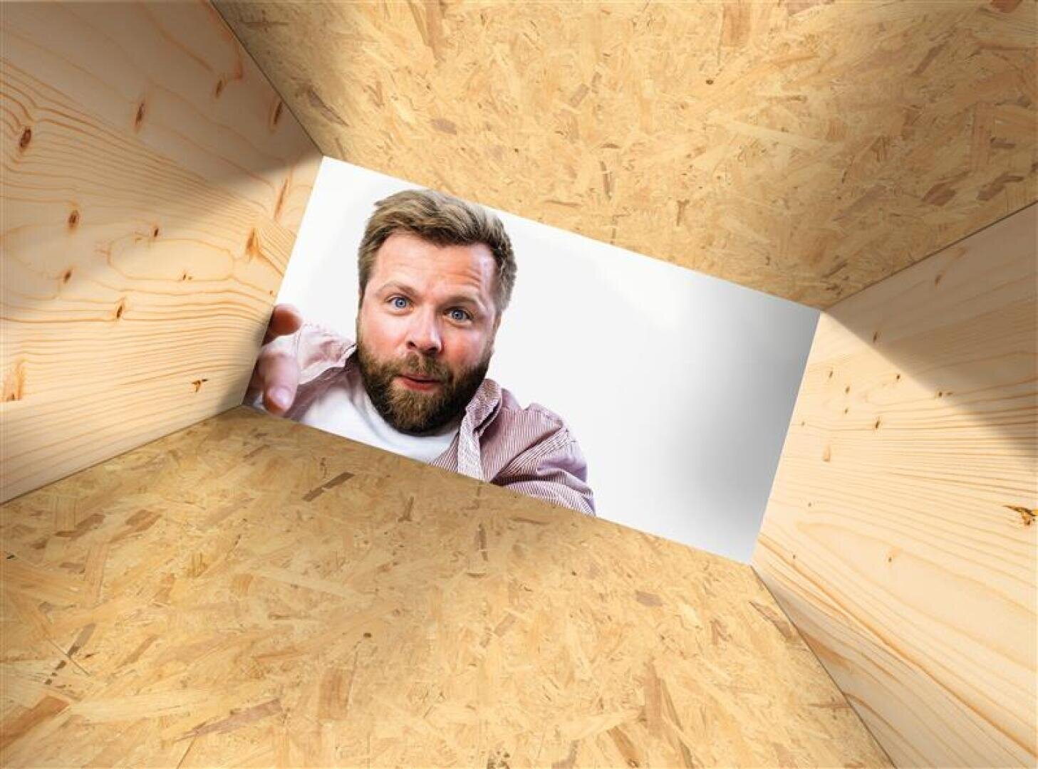 Ein Mann mit Bart und legerem Hemd blickt von oben in eine Holzkiste hinab, wobei er mit der Hand in die Kamera greift. Die Kiste hat helle, holzgemaserte Wände und einen hellen, weißen Hintergrund außen.