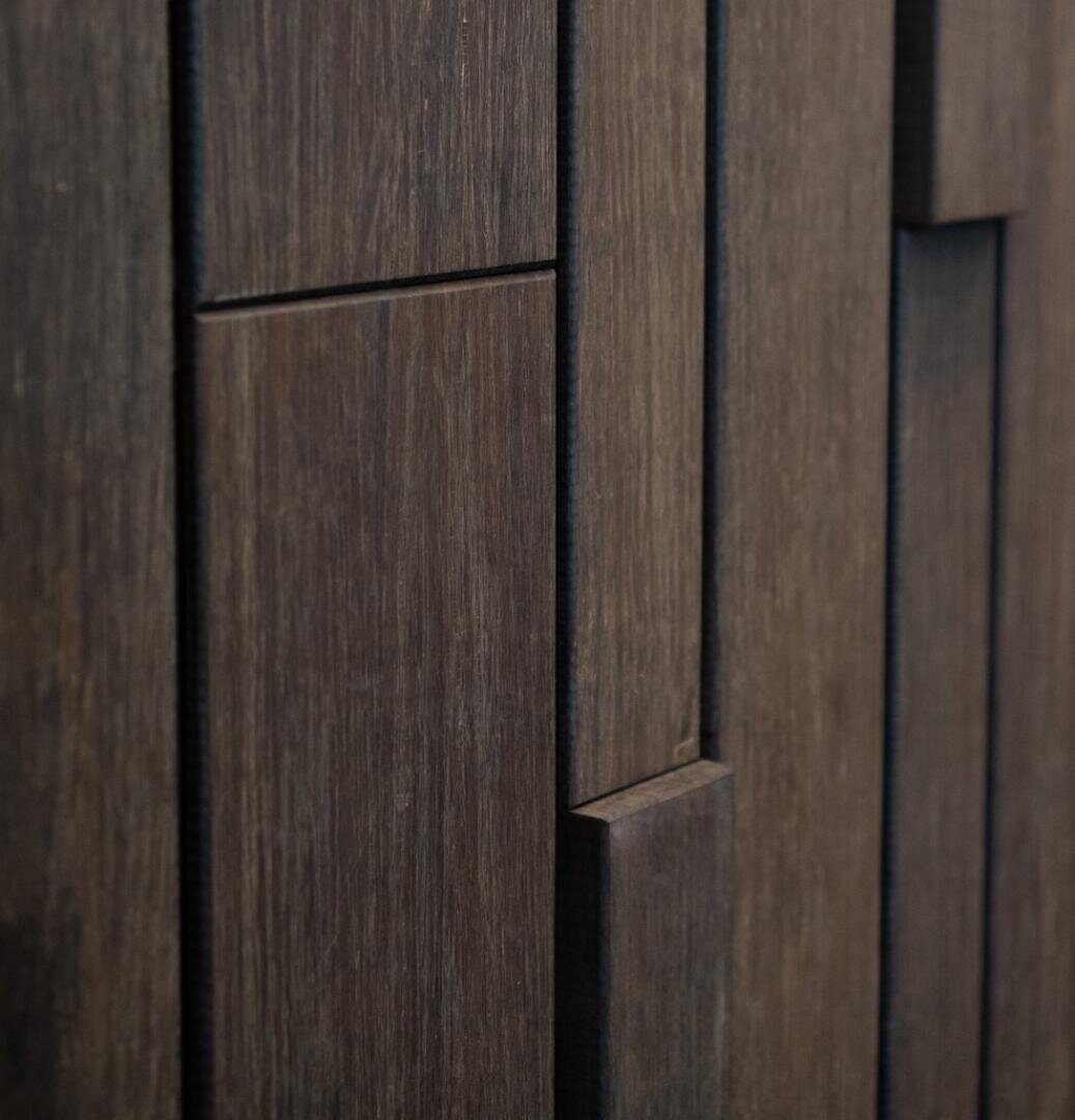 Nahaufnahme einer dunklen Holzoberfläche mit vertikalen rechteckigen Platten unterschiedlicher Breite und Tiefe, die ein geometrisches und strukturiertes Muster ergeben.