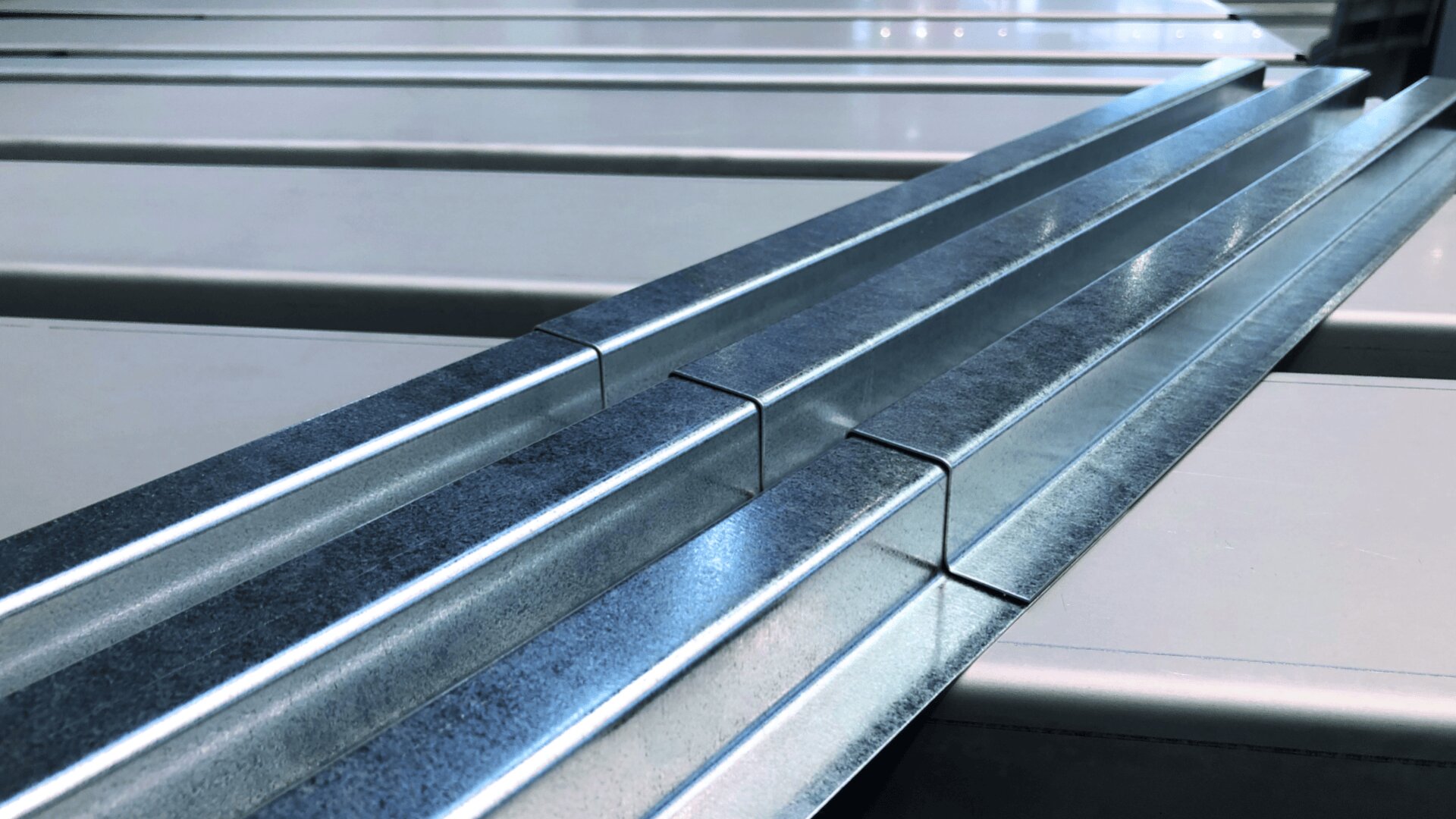 Nahaufnahme paralleler Metallträger oder -schienen mit silberner Oberfläche, die auf einer hellen Oberfläche ausgerichtet sind und ein geometrisches und industrielles Muster erzeugen.