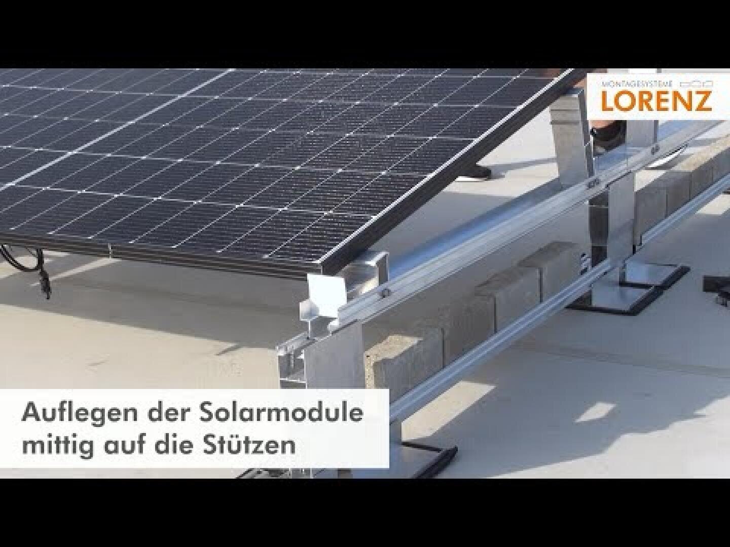 Nahaufnahme von Solarmodulen, die auf einem Metallrahmen installiert werden, wobei Betonblöcke als Stütze dienen. Der deutsche Text lautet: Auflegen der Solarmodule mittig auf die Stützen. Logo der Firma Lorenz in der oberen rechten Ecke.