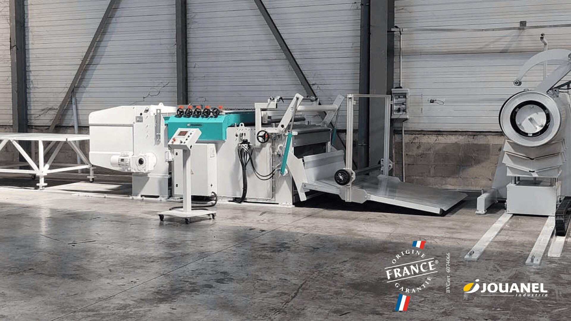 Industrielle Metallbearbeitungsmaschinen in einer Lagerhalle, darunter eine Blechbearbeitungsmaschine und ein Bedienfeld. Der Boden ist aus Beton, die Wände sind aus Wellblech. Die Zertifizierungslogos von Jouanel und France sind sichtbar.