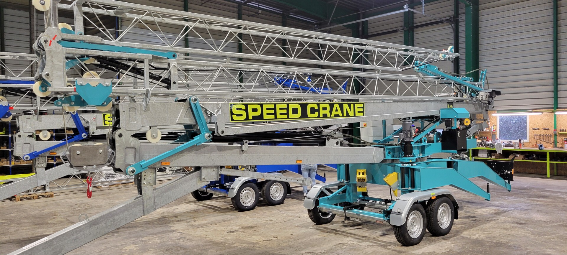 Ein großer mobiler Schnellkran mit ausgefahrenem Gittermastausleger steht in einem Innenbereich auf einem Betonboden und ist mit Rädern und einem SPEED CRANE-Etikett an der Seite versehen.
