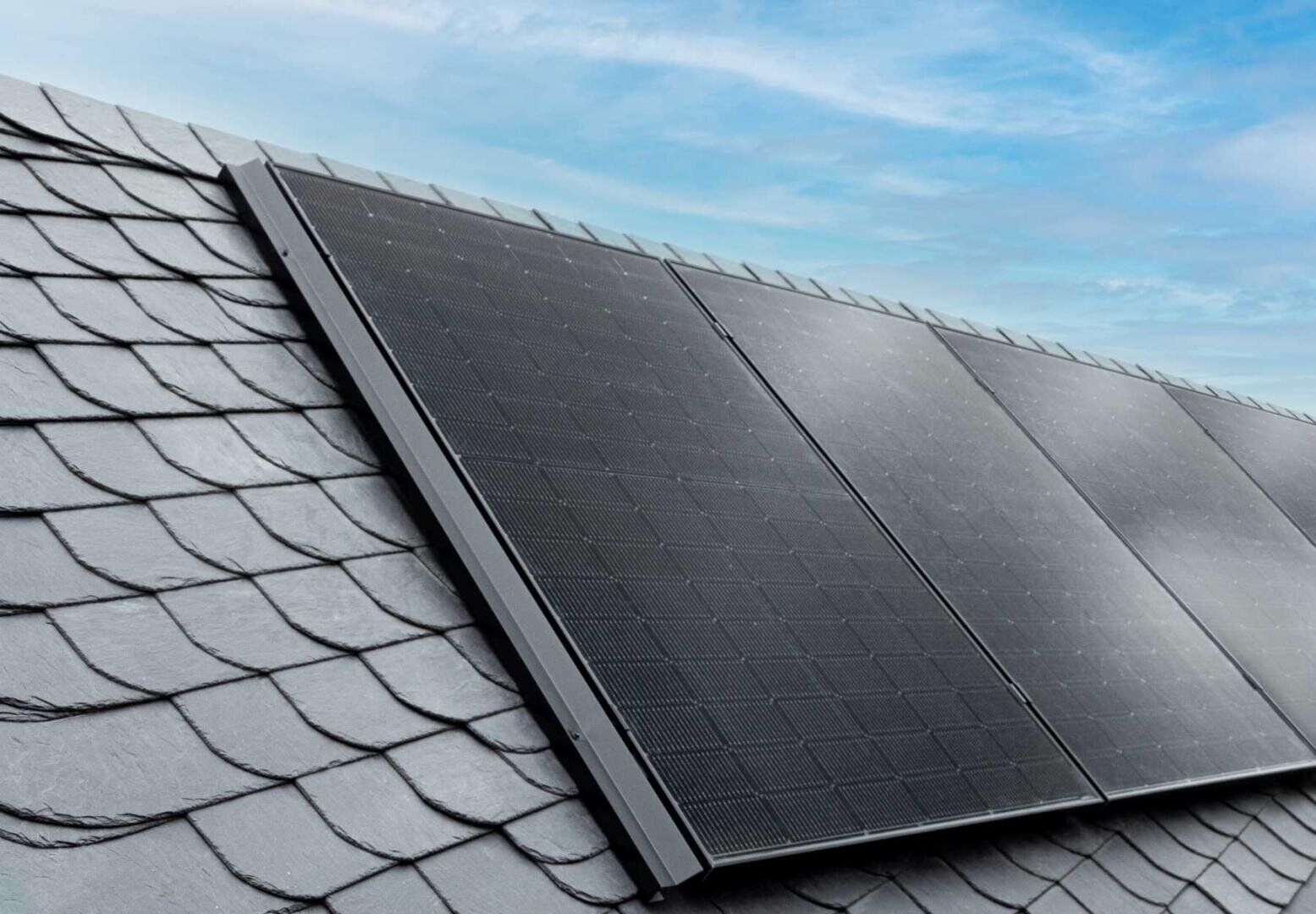 Vier Sonnenkollektoren sind auf einem grauen Schindeldach unter einem blauen Himmel mit leichten Wolken installiert.
