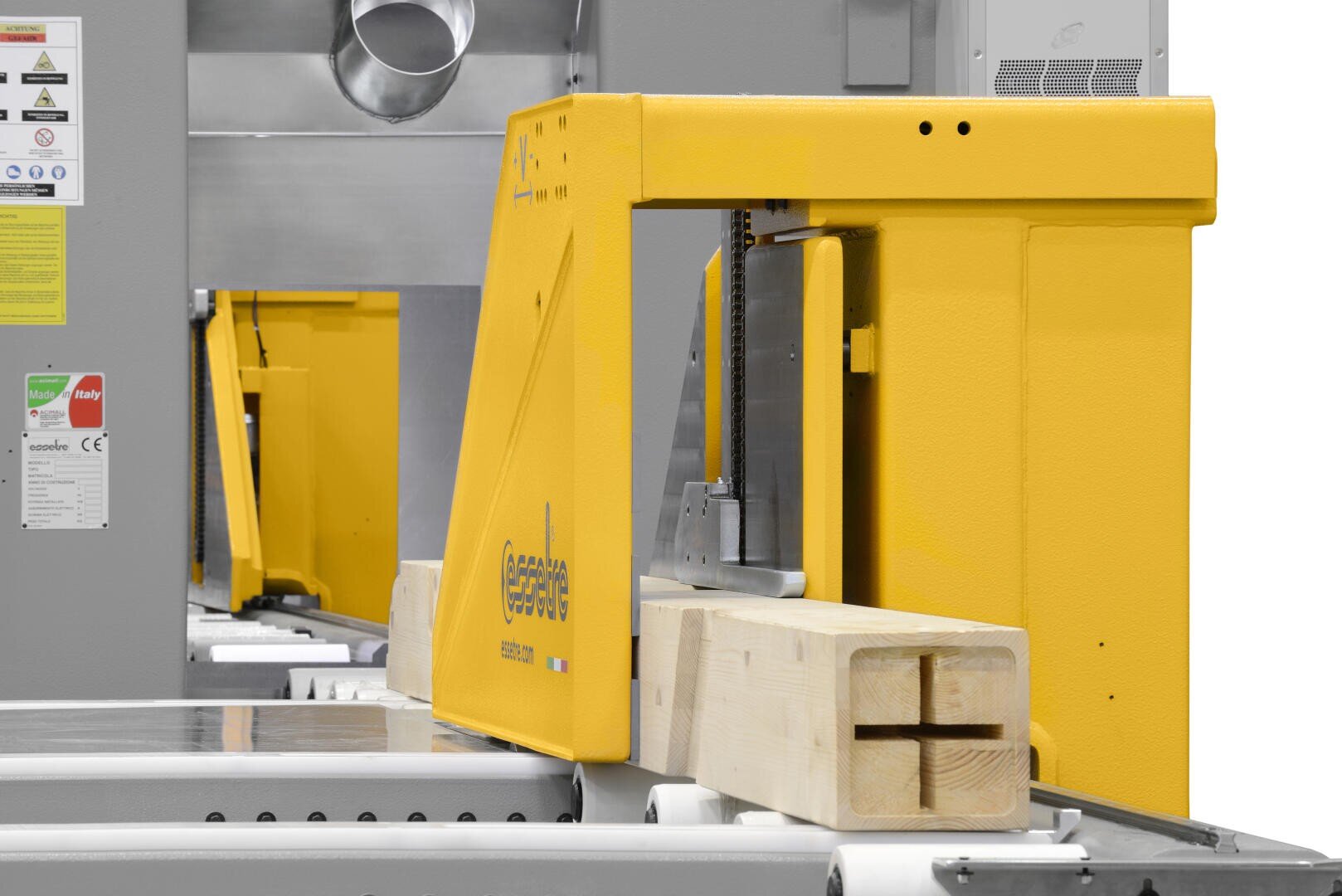 Eine Nahaufnahme einer gelben industriellen Holzbearbeitungsmaschine, die in einer Fabrik einen rechteckigen Holzbalken mit einer kreuzförmigen Nut schneidet.