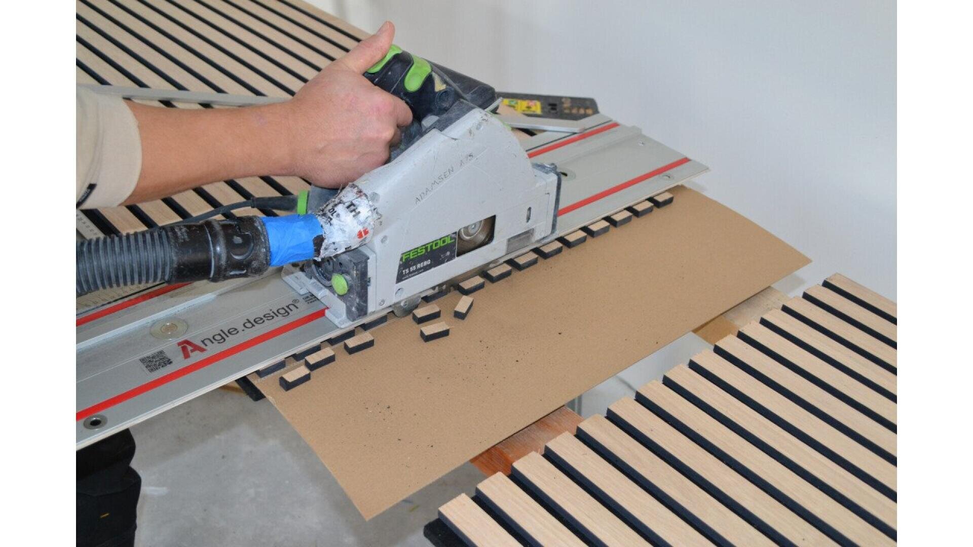 Eine Person verwendet eine elektrische Säge mit Führungsschiene, um Nuten in eine Holzplatte auf einer Arbeitsfläche aus Lattenrost zu sägen. Die Säge erzeugt beim Überfahren des Bretts rechteckige Schlitze.