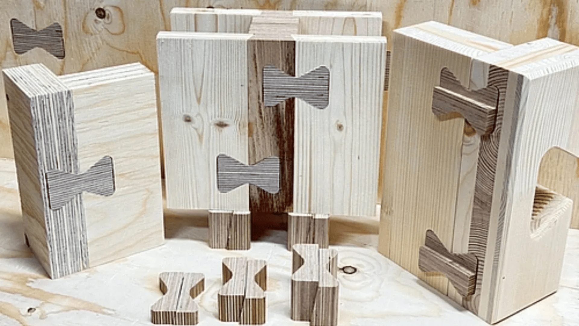 Mehrere Holzklötze sind mit schmetterlingsförmigen Holzstiften verbunden und demonstrieren so verschiedene Verbindungstechniken in der Holzverarbeitung. Der Hintergrund ist eine helle Holzoberfläche.
