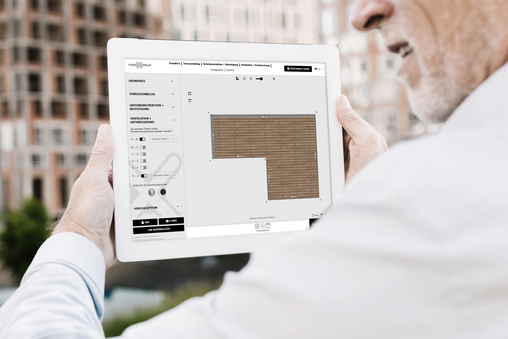 A person holds a tablet on which a room planning or design software with a wooden pattern grid is displayed, outdoors with blurred buildings in the background.
