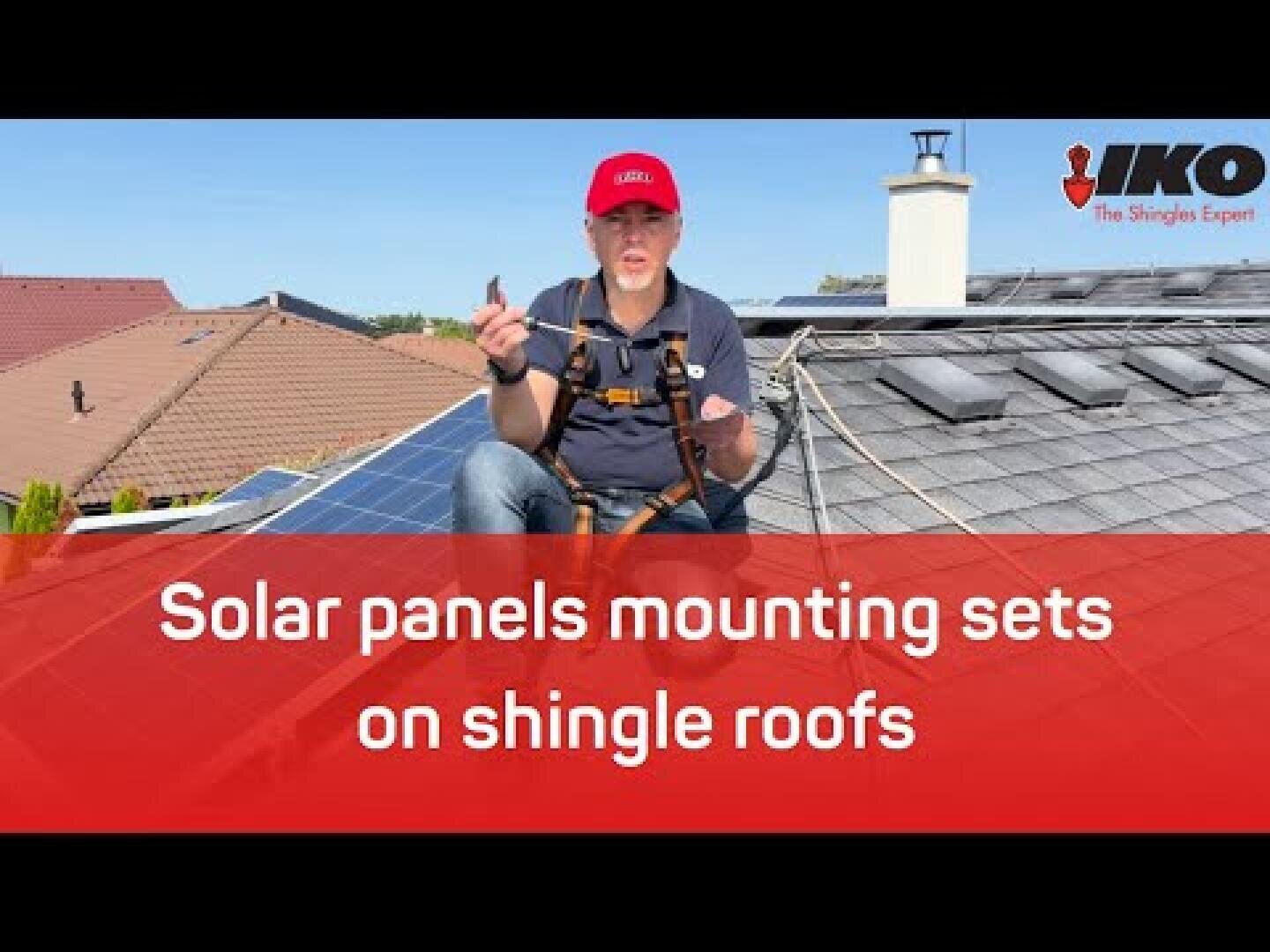 A person wearing safety gear sits on a shingle roof with solar panels, holding installation tools. The text reads: Solar panels mounting sets on shingle roofs. The IKO logo appears in the top right corner.