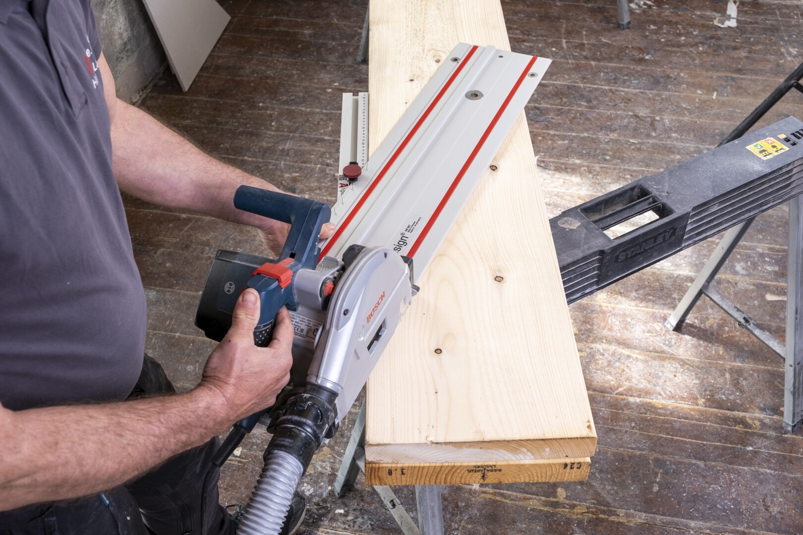 A person operates a circular saw with a guide rail to cut a wooden plank on a workbench in a workshop setting.