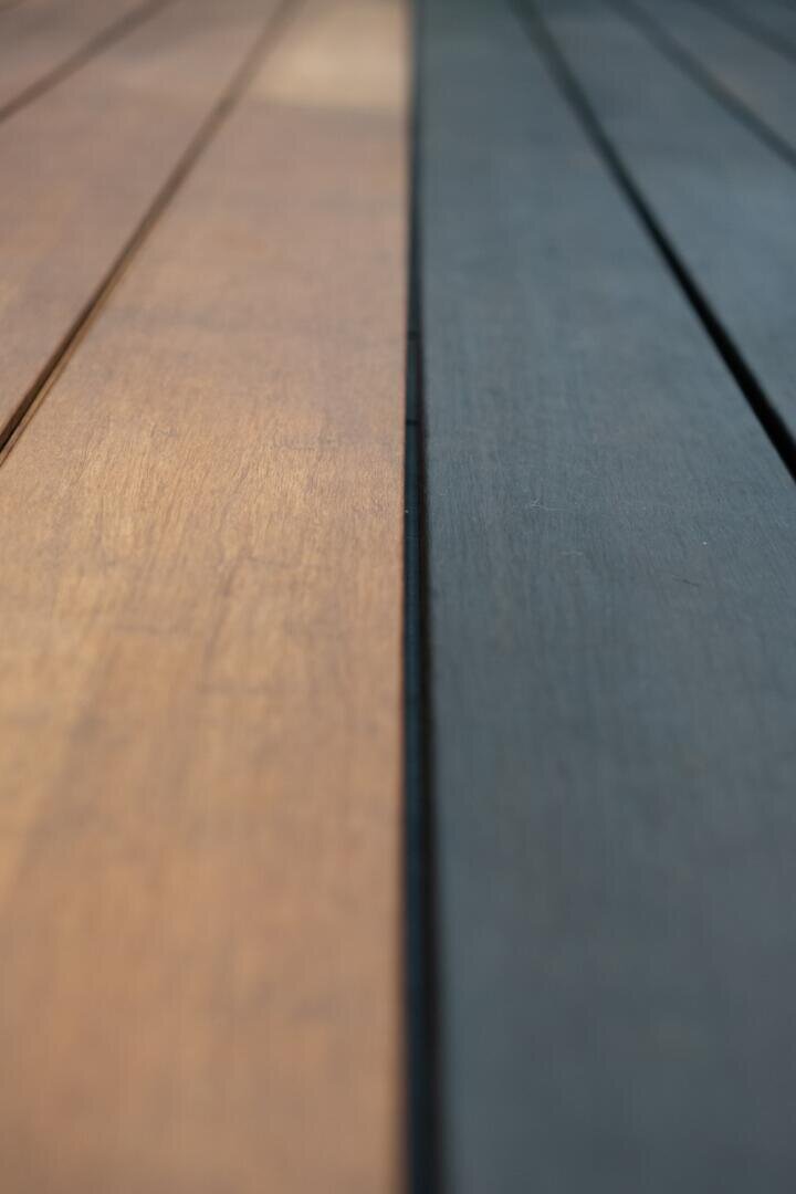 Close-up of a wooden surface with boards split in the middle; the left side is light brown, the right side darker, suggesting different lighting, treatment or age.