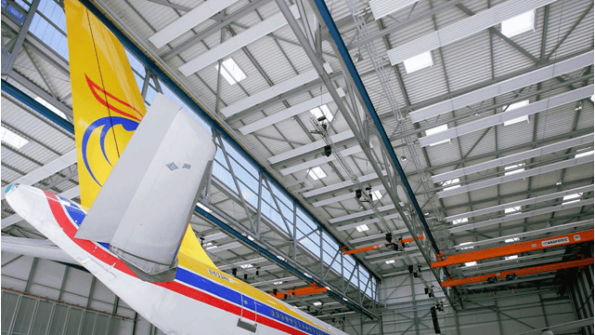 Das Heck eines Verkehrsflugzeugs mit farbenfrohem Design befindet sich in einem geräumigen, modernen Flugzeughangar, in dem Metallträger und Brückenkräne sichtbar sind.