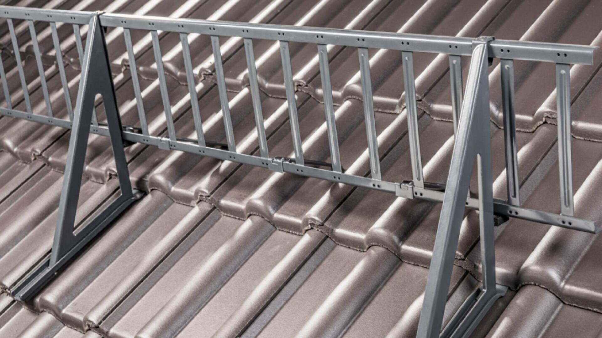 Auf einem braunen, mit Ziegeln gedeckten Schrägdach wird ein Schneefanggitter aus Metall angebracht, um das Abrutschen von Schnee zu verhindern.