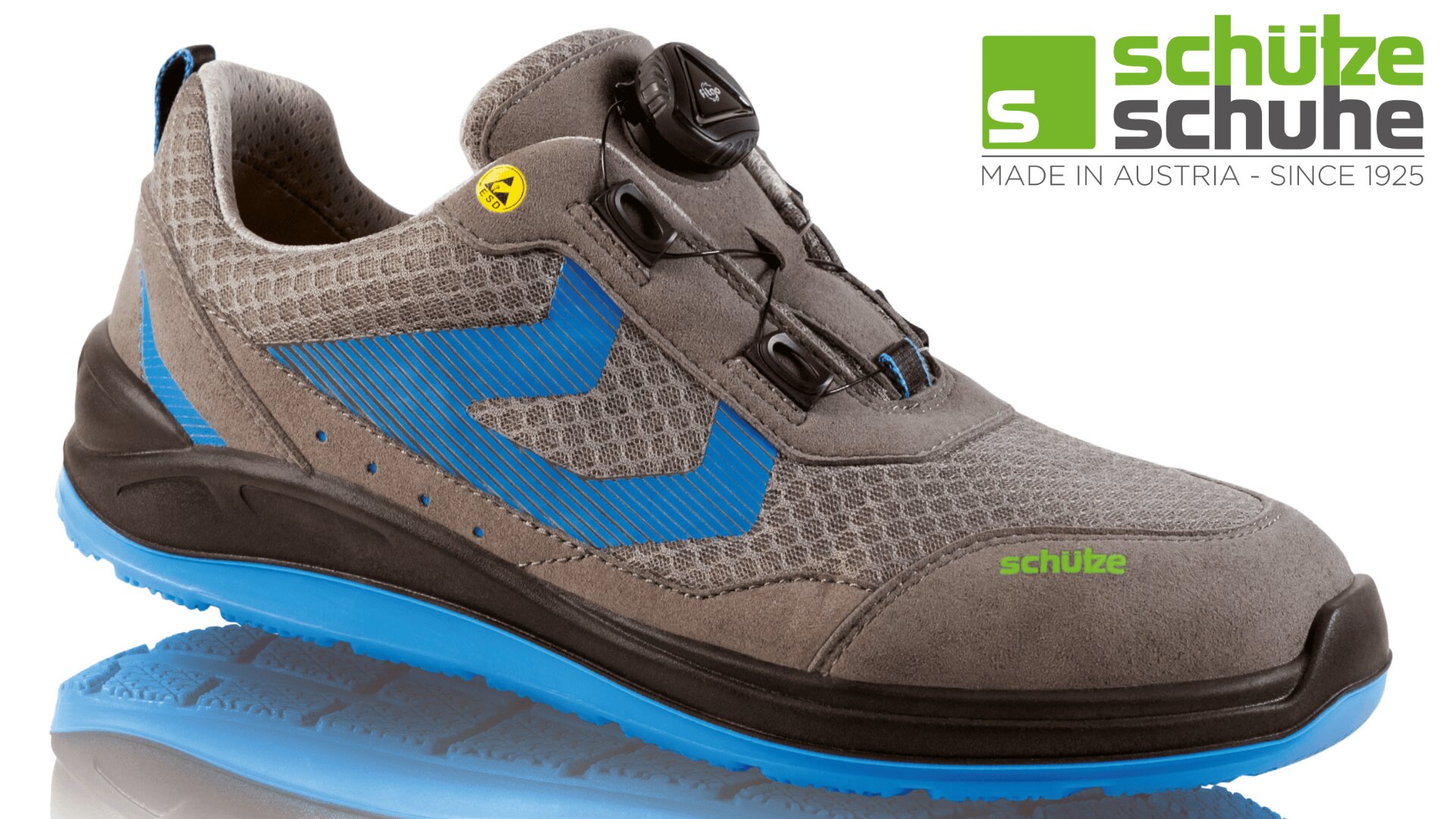 Grau-blauer Arbeitsschuh im Sportstil mit Mesh-Obermaterial, schwarzem Drehverschluss und blauer Laufsohle. Das Schütze Schuhe-Logo und der Text „Made in Austria – Since 1925“ erscheinen in der oberen rechten Ecke.