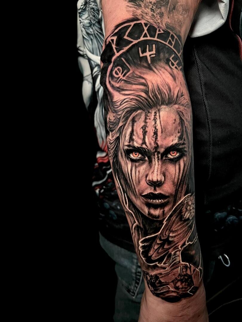 Ein detailliertes schwarz-graues Unterarmtattoo einer wilden Frau mit leuchtenden orangefarbenen Augen, Runen über ihrem Kopf und einem Raben unter ihrem Gesicht, alles in einem realistischen Stil ausgeführt.