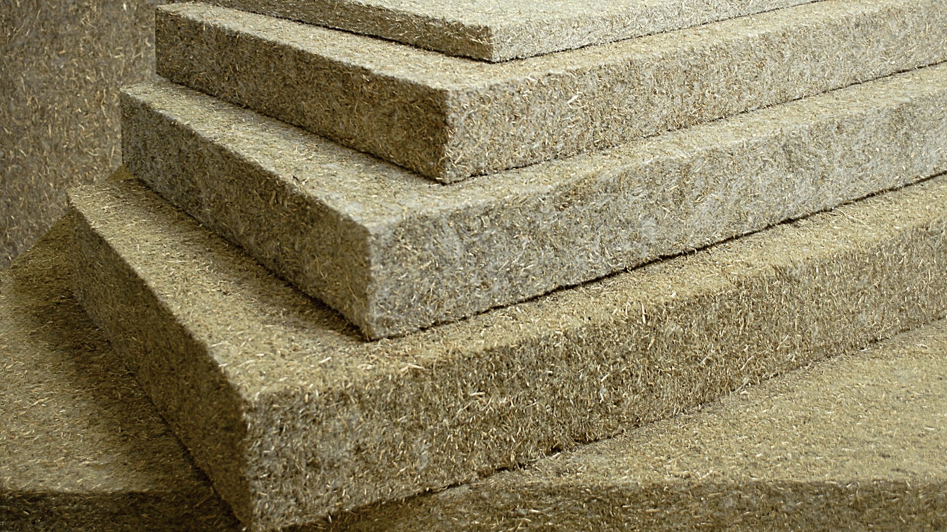 Eine Nahaufnahme mehrerer gestapelter rechteckiger Platten aus komprimierten Naturfasern, möglicherweise Hanf oder Stroh, die zu Dämm- oder Bauzwecken verwendet werden. Die Platten haben eine raue, strukturierte Oberfläche.
