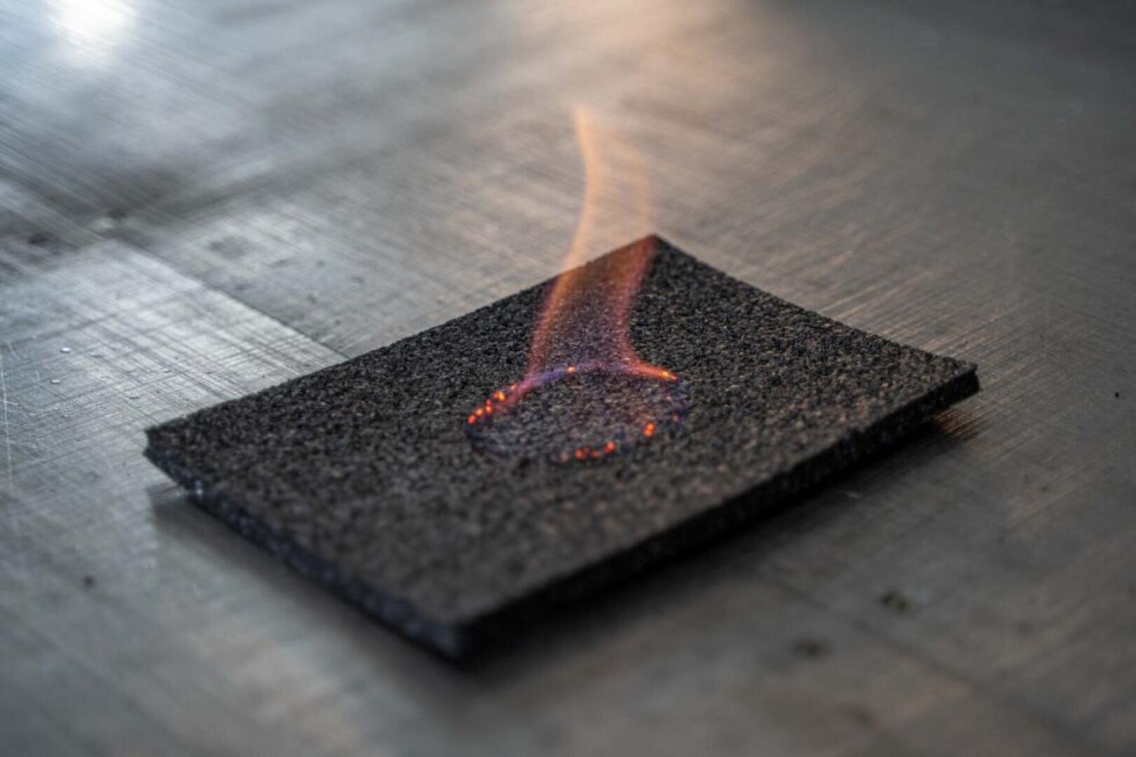 In the center burns a rectangular piece of dark, textured material with a small orange flame and embers resting on a metallic surface.