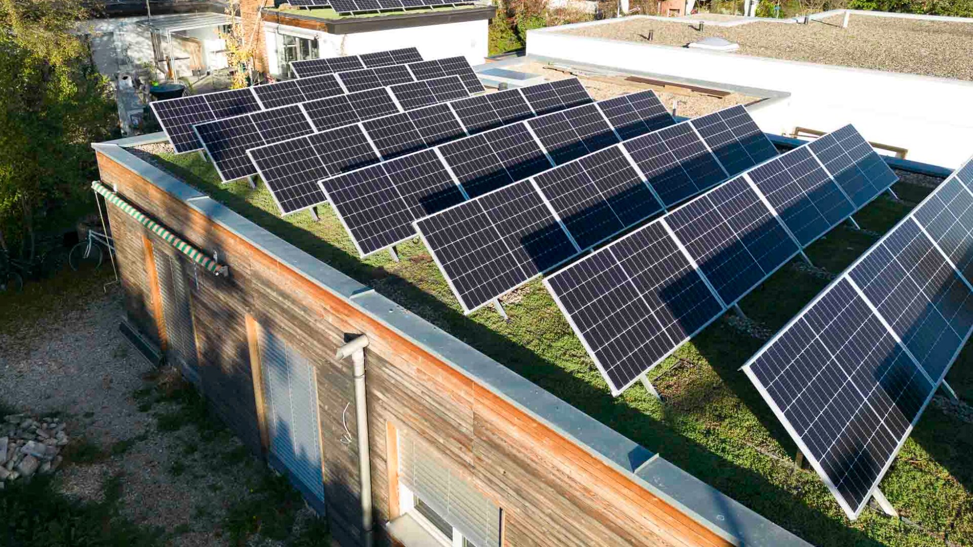 Auf dem flachen, begrünten Dach eines modernen Gebäudes sind Solarmodule montiert, die an sonnigen Tagen das Sonnenlicht einfangen und so erneuerbare Energie erzeugen.