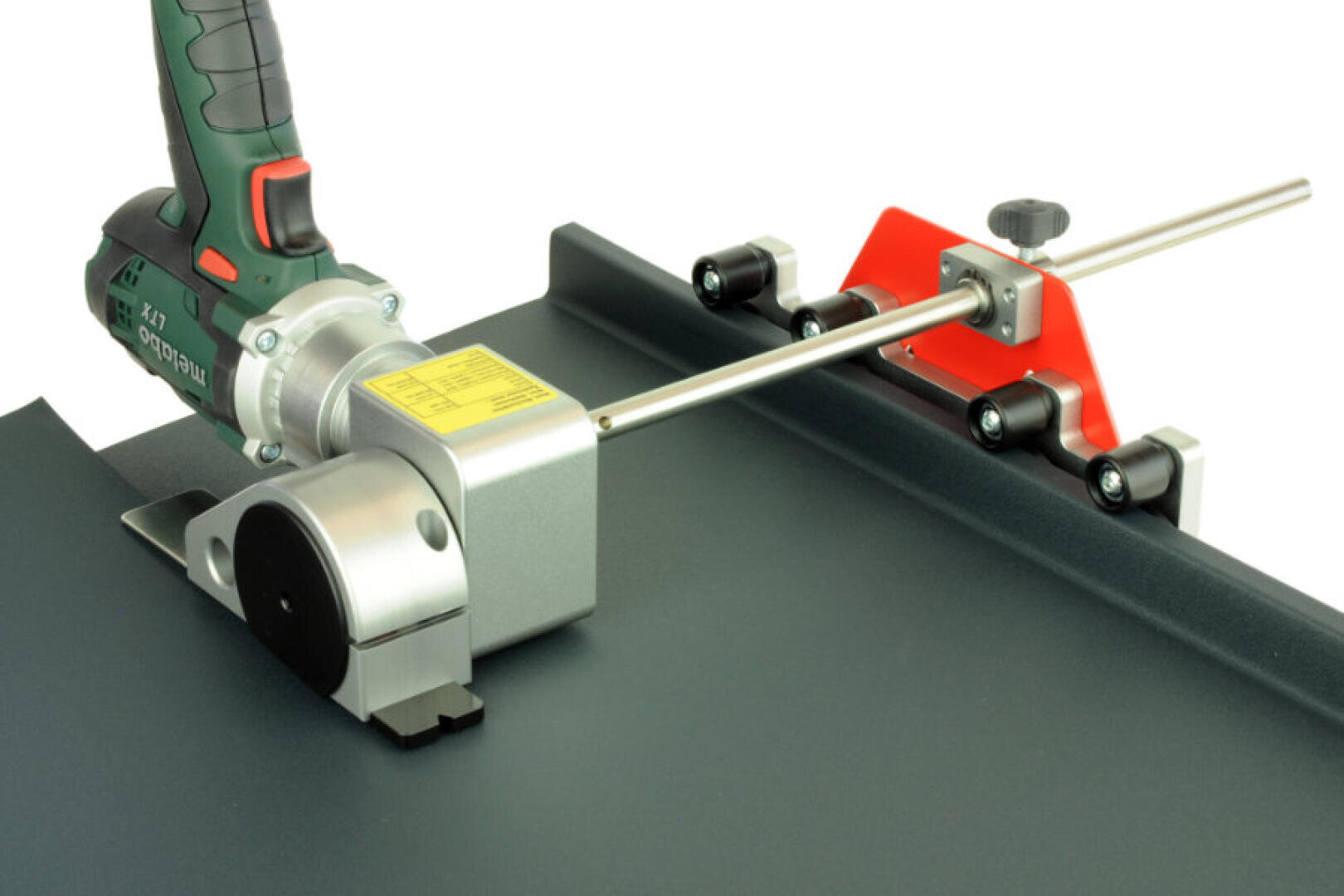 Nahaufnahme eines Metallschneidewerkzeugs mit Akkuantrieb, das ein profiliertes Stück Blech schneidet und mit einem rot-silbernen Führungsschienensystem ausgerichtet ist.