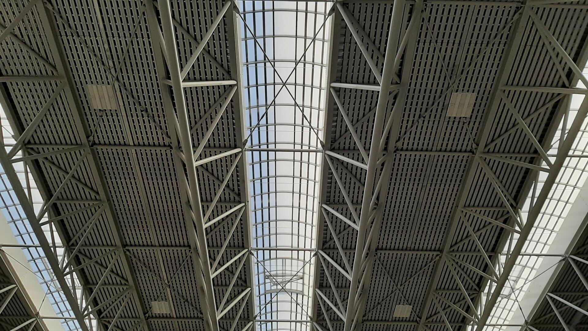 Blick auf eine große Industriedecke mit Metallträgern, -trägern und -platten und einem zentralen Abschnitt aus durchscheinendem Material, durch das natürliches Licht einfällt.