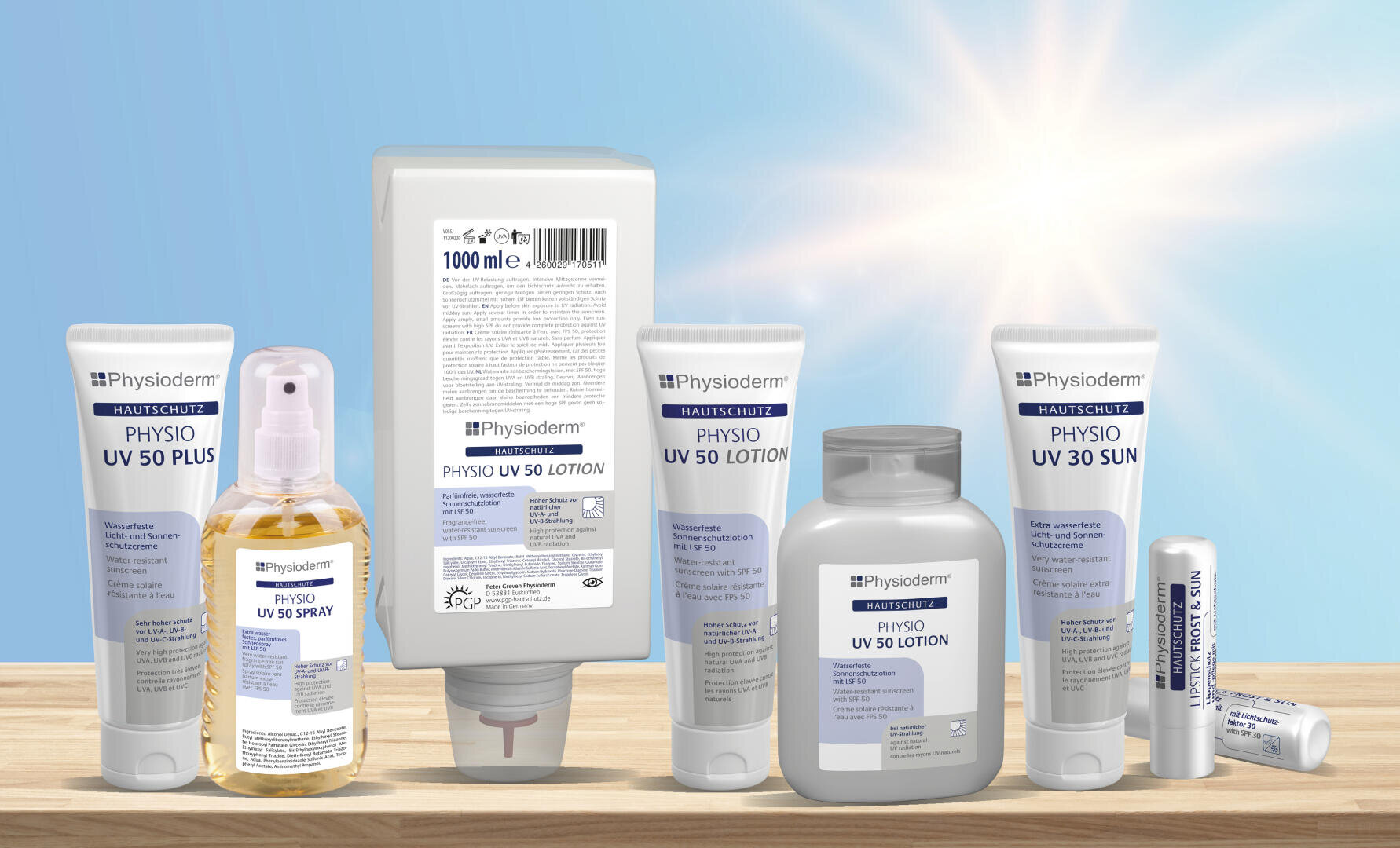 Mehrere Physioderm-Sonnenschutzprodukte, darunter Lotionen, Sprays und Stifte, sind auf einer Holzfläche mit einer hellen Sonne und einem blauen Himmel im Hintergrund angeordnet. Die Produkte sind mit SPF 30 und SPF 50 beschriftet.