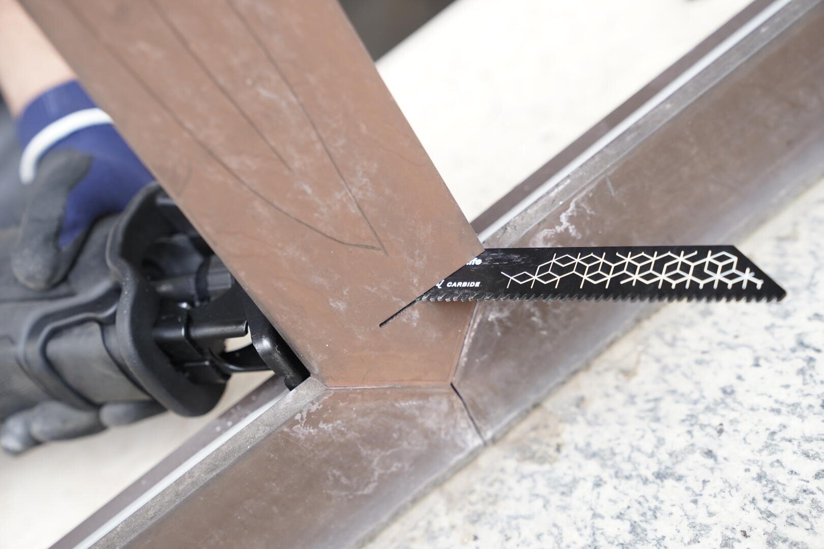 Eine behandschuhte Hand verwendet eine Säbelsäge mit einem schwarzen Hartmetallblatt, um einen Metallträger an einer Gehrungsverbindung auf einer Arbeitsfläche zu durchtrennen.