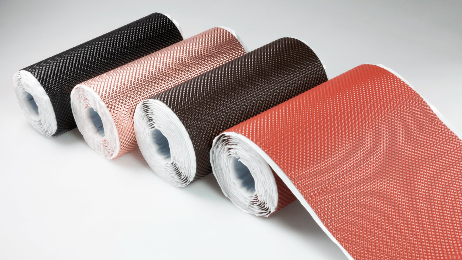 Four rolls of textured, flexible material in shades of black, brown, and reddish-orange, laid out side by side on a white surface, with the ends partially unrolled.