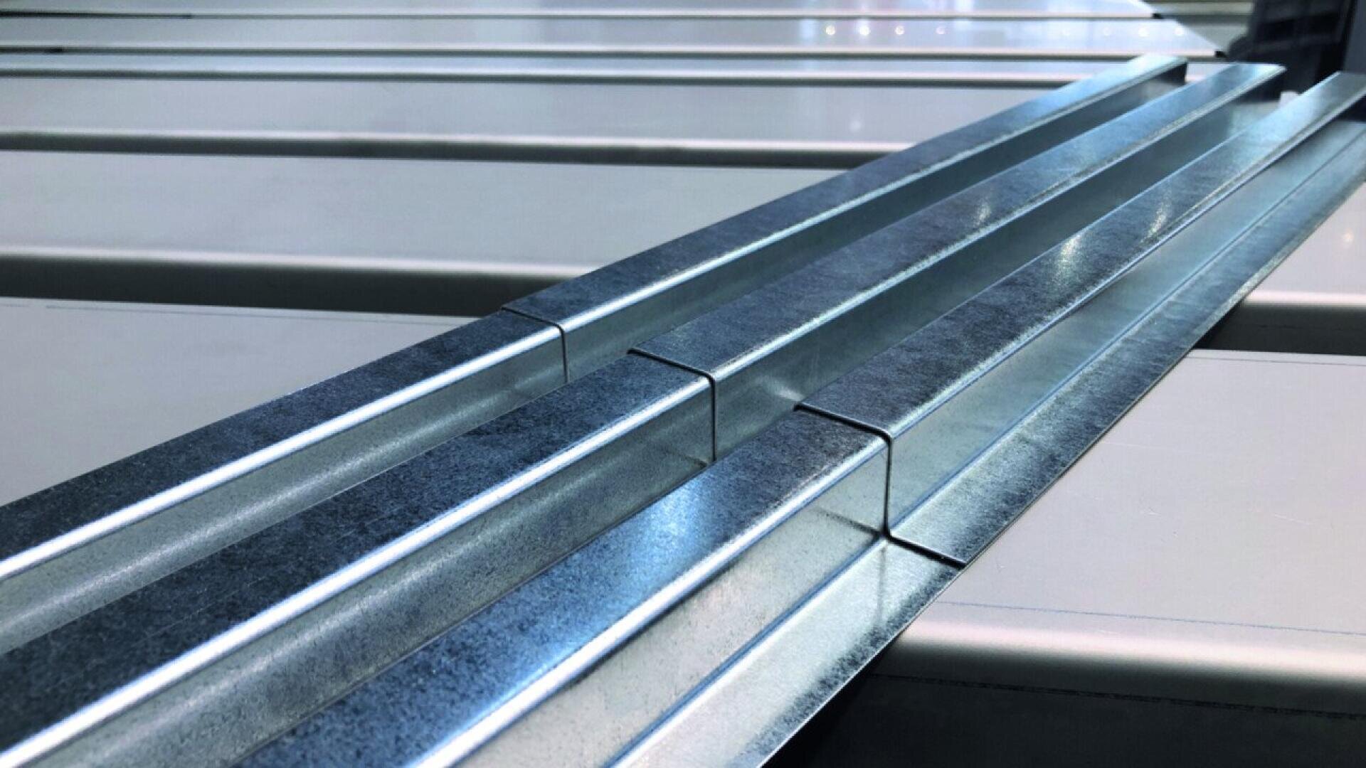 Close-up of parallel metal rails or beams with a reflective surface, aligned on a light-colored flat background, creating a pattern of straight lines and angles.