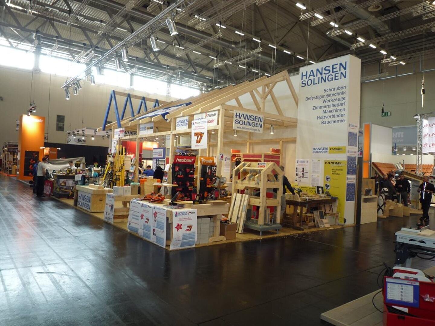 Ein Messestand mit Holzrahmen und ausgestellten Bauwerkzeugen. Auf den Schildern steht "Hansen Solingen". In einer großen, gut beleuchteten Halle gehen die Menschen umher und begutachten die Produkte auf der Ausstellung.