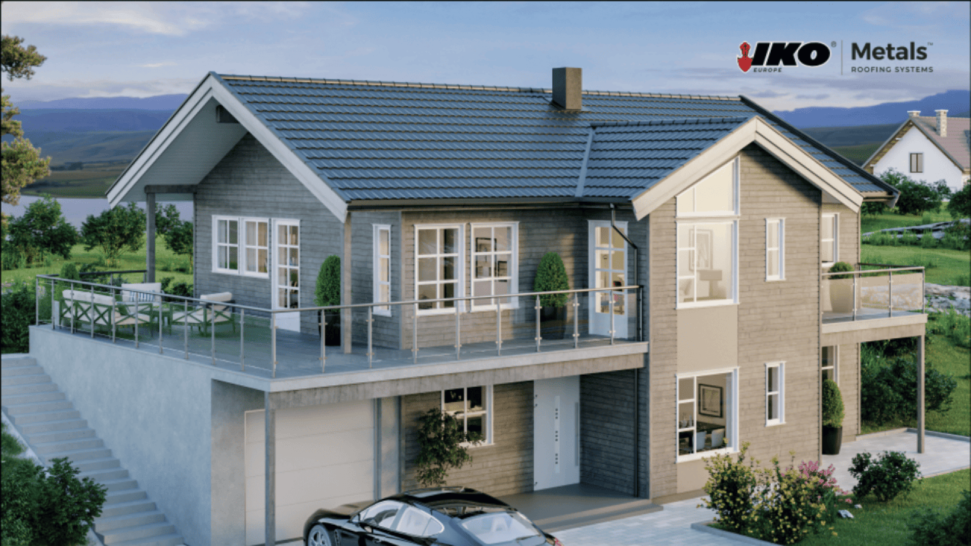 A modern two-story house with large windows, a balcony, and a grey tiled roof. A car is parked in the driveway, and the house is surrounded by greenery. The IKO Metals logo appears in the upper right corner.